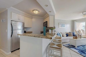 A modern kitchen with white cabinetry, a stainless steel refrigerator, and a built-in island with bar stools. - Makai 108 (Ocean City)