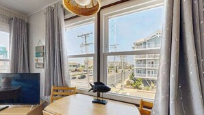 A room with a TV, wooden table, and a view of buildings and power lines through large windows. - Well-Equipped Beach Condo near the Ocean w/Private Balcony, Central A/C, W/D (Ocean City)
