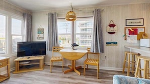 A room with a TV, wooden table, chairs, a hanging light fixture, and a view of buildings outside. - Well-Equipped Beach Condo near the Ocean w/Private Balcony, Central A/C, W/D (Ocean City)