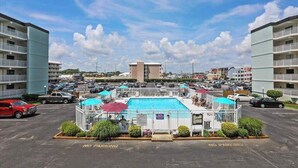 A hotel with a swimming pool, multiple floors, and a parking area with a 'No Parking' sign. - Ocean Block Condo w/ Side Ocean View, Balcony, WiFi, AC & Shared Pool (Ocean City)
