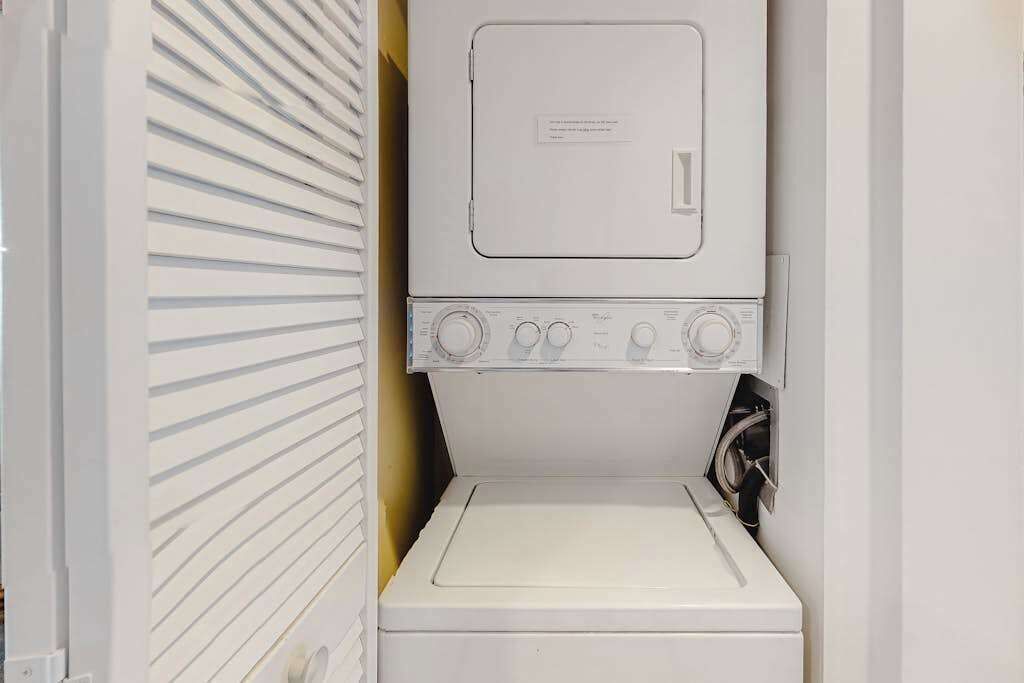 A compact laundry room with a stacked washer and dryer, a small ironing board, and a wall-mounted towel rack.