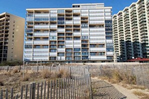 A multi-story residential building with a grid of balconies, a sandy foreground, and a clear blue sky. - Highpoint North 12G (Ocean City)
