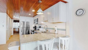 Eine moderne Küche mit weißen Schränken, einer Granit Arbeitsplatte, einem Edelstahlkühlschrank und einer Holzbalkendecke.