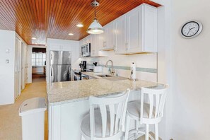 A modern kitchen with white cabinets, a granite countertop, a stainless steel refrigerator, and a wooden ceiling. - Highpoint North 12G (Ocean City)
