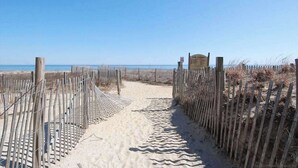 Ein Sandweg am Strand mit Holzzaun, der zu einem Strandabschnitt führt.