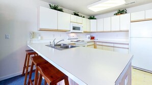 Une cuisine moderne avec des meubles blancs, un îlot central doté de tabourets, un four à micro-ondes et une cuisinière.