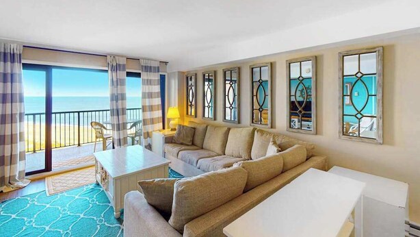 Habitación de hotel con balcón, sofá, mesa y marcos de ventana decorativos.