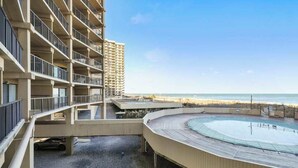 Un hotel de varios pisos con zona de piscina, mobiliario exterior y vistas a la playa.