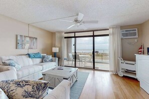 A spacious living room with a white sofa, a coffee table, and a view of the ocean through large sliding glass doors. - Exquisite beachfront condo with pool & beach views & balcony (Ocean City)