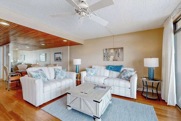 A modern living room with two white sofas, a wooden coffee table, and a ceiling fan. - Exquisite beachfront condo with pool & beach views & balcony (Ocean City)