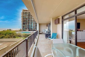 A balcony with a view of a high-rise building, a pool, and a dining area with chairs and tables. - Exquisite beachfront condo with pool & beach views & balcony (Ocean City)