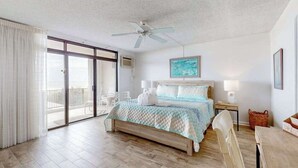 Ein Schlafzimmer mit Bett, Deckenventilator, Gemälde, Fenster und Balkon.