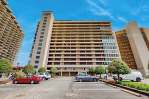 A multi-story hotel with a central courtyard, parking area, and a clear blue sky. - Exquisite beachfront condo with pool & beach views & balcony (Ocean City)