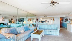 Ein geräumiges Wohnzimmer mit gestreiften Sofas, einem Couchtisch und einer Küche im Hintergrund.