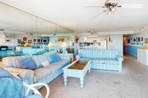 A spacious living room with striped sofas, a coffee table, and a kitchen in the background. - Inviting beachfront condo with beach views, balcony, AC & washer/dryer (Ocean City)
