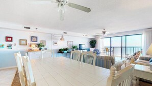 Ein Essbereich mit einem weißen Tisch und Stühlen, eine Küche im Hintergrund und ein Balkon mit Blick.