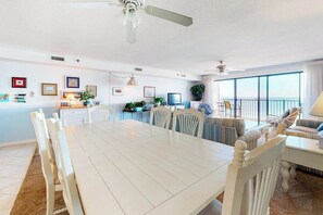 A dining area with a white table and chairs, a kitchen in the background, and a balcony with a view. - Inviting beachfront condo with beach views, balcony, AC & washer/dryer (Ocean City)
