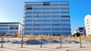 Ein mehrstöckiges Gebäude mit einer rasterartigen Fassade, gelegen in einer sandigen, wenig bewachsenen Gegend.