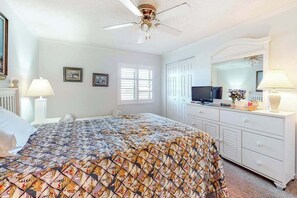 Quarto com cama, penteadeira, televisão e ventoinha no teto.