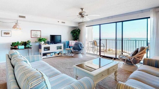 Ein geräumiges Wohnzimmer mit einer Couch, Sesseln, einem Couchtisch, einem Fernseher und einem Balkon mit Blick.