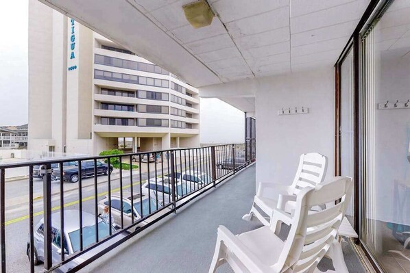 A balcony with white chairs, a view of a parking lot, and a building with a sign. - Grandview 203 (Ocean City)