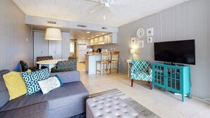 A modern living room with a sofa, ottoman, teal cabinet, and a flat-screen TV. - Grandview 203 (Ocean City)