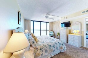 A bedroom with a bed, a ceiling fan, a TV, a dresser, and a window with curtains. - Affordable beach condo with balcony views, pools & game room (Ocean City)