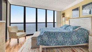 A bedroom with a large window, a bed, a chair, and a bedside table. - Cozy beachfront condo with balcony, washer/dryer, pools & gym (Ocean City)