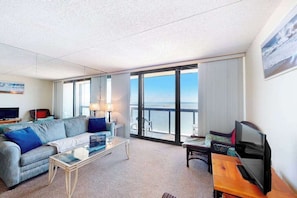 Ein Hotelzimmer mit großem Balkon, einer Couch, einem Fernseher und einem Couchtisch.