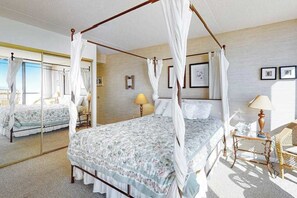 Uma cama com dossel com colcha florida, uma mesa de cabeceira com abajur e uma cadeira.