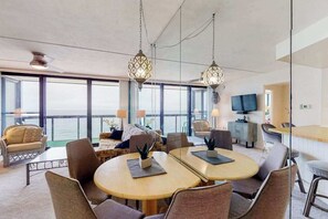 Ein modernes Hotelzimmer mit einem großen Fenster, einer Essecke mit runden Tischen und einem Fernseher.