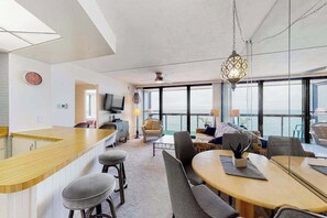 Ein modernes Interieur mit Küchenbar, Essbereich und Sitzgelegenheiten an großen Fenstern mit Meerblick.