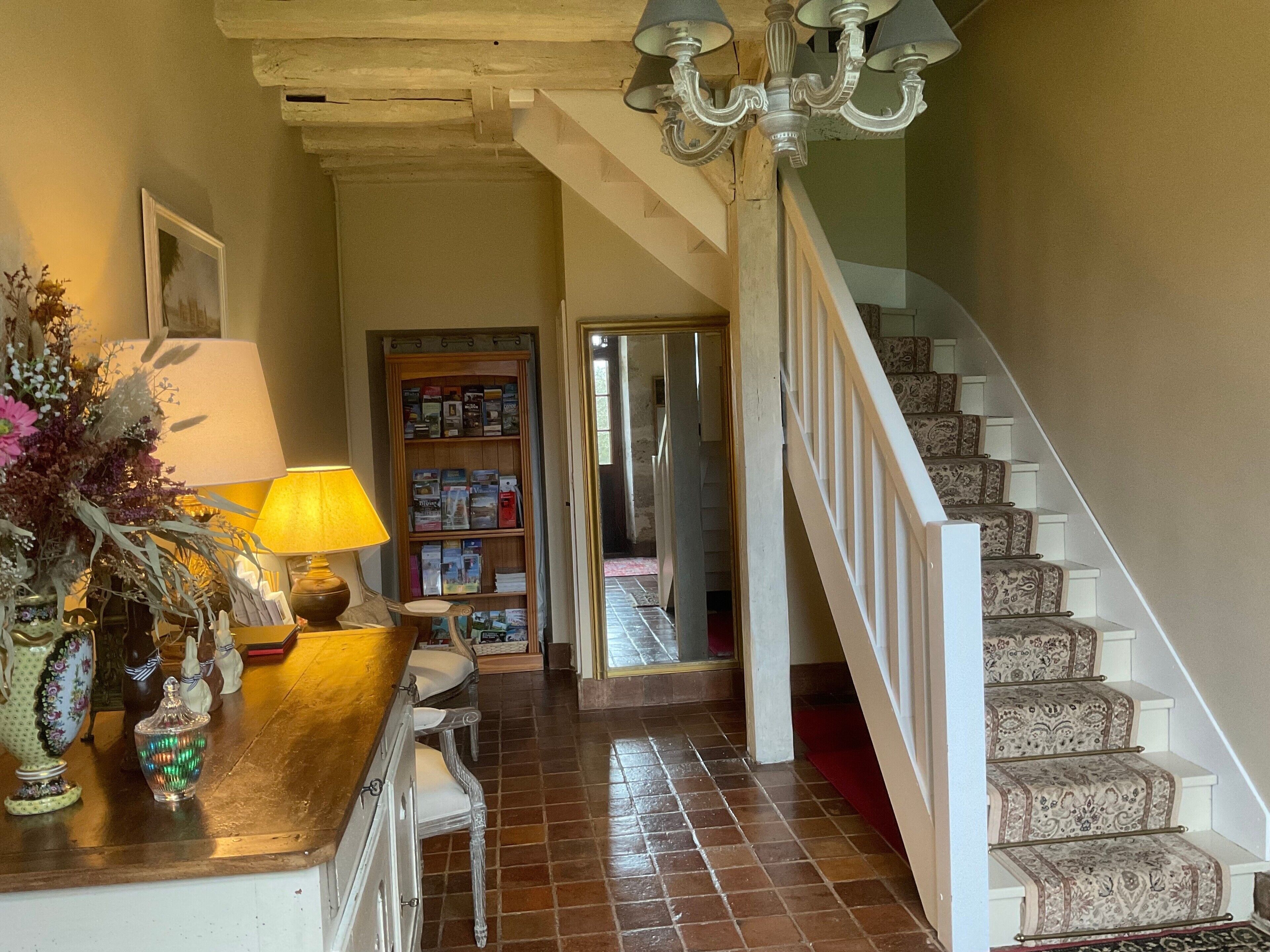 A staircase with patterned carpet leading to an upper floor, a wooden bookcase with books, a lamp, and decorative items on a wooden table.