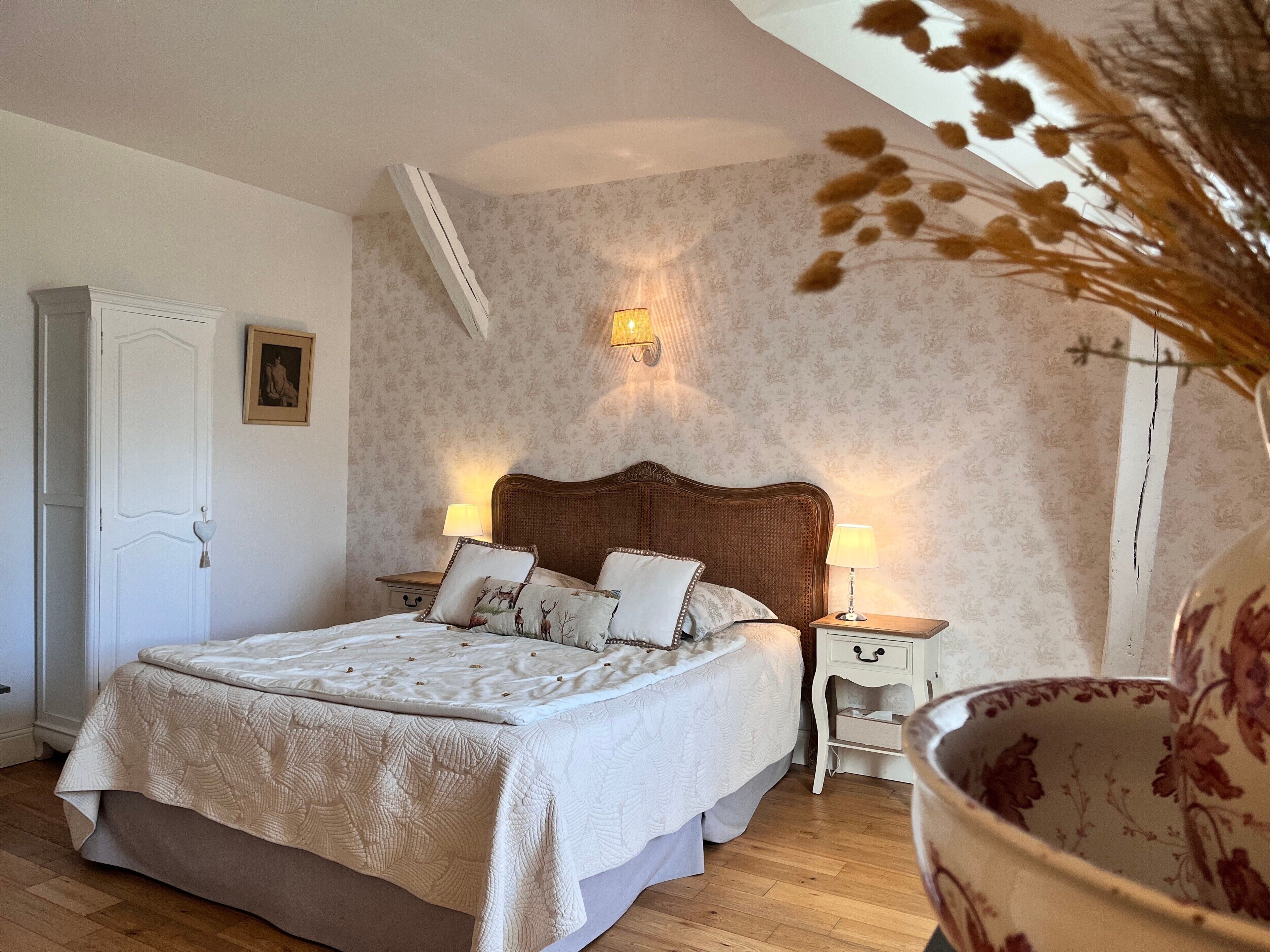 Une chambre à coucher avec un grand lit, deux tables de chevet, une lampe fixée au mur et une porte dotée d’une poignée.