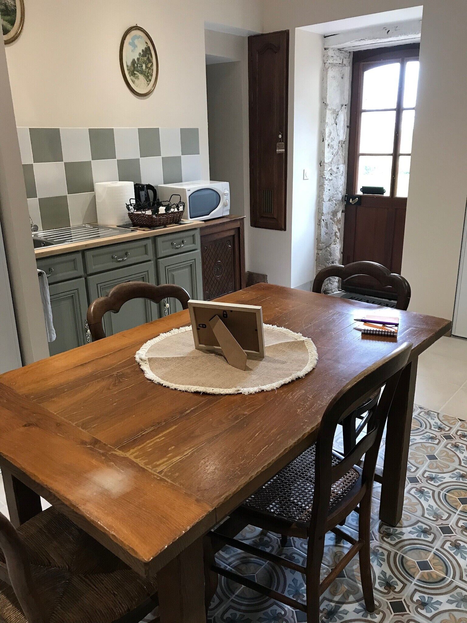 Een eettafel met stoelen, een keuken met een magnetron, en een deur naar buiten.