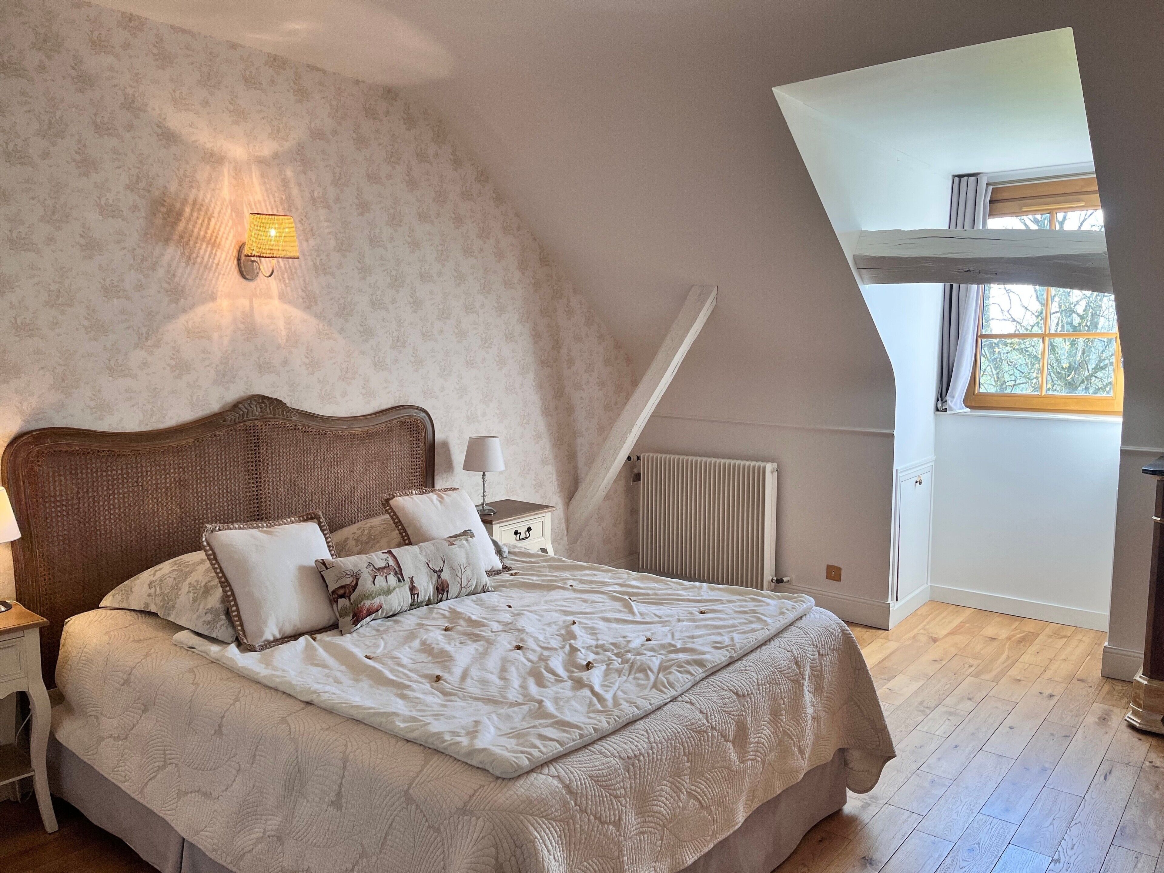 A bedroom with a sloped ceiling, a bed with patterned bedding, a nightstand with a lamp, and a radiator.