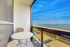 A balcony with a view of the beach, a table, and two wicker chairs. - Fascinating beachfront studio with great balcony views, pools, gym & AC (Ocean City)