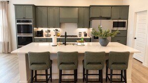 Una cocina moderna con una isla grande, electrodomésticos integrados y taburetes de bar verdes.