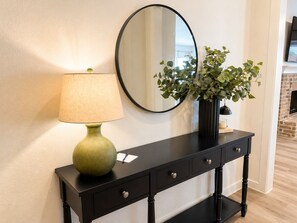 A black console table with a green lamp, a mirror, and a vase with green foliage.