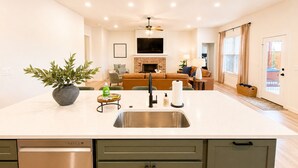 Una cocina moderna con una isla central, un comedor con mesa y sillas, una sala de estar con sofá y una chimenea.
