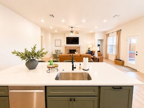 A modern kitchen with a central island, a dining area with a table and chairs, a living room with a sofa, and a fireplace. - Backyard Escape | Hot Tub + Fire Pit (Lubbock)