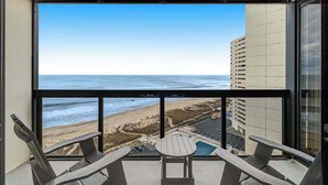 Un balcón con vista a la playa y al océano, dos sillas y una mesita.
