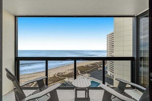 A balcony with a view of the beach and ocean, two chairs, and a small table. - Coastal-themed beachfront condo with angled ocean views & pools (Ocean City)