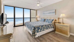 Un dormitorio con una cama grande, un escritorio, una mesita de noche y vista al océano.
