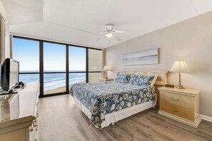 A bedroom with a large bed, a desk, a nightstand, and a view of the ocean. - Coastal-themed beachfront condo with angled ocean views & pools (Ocean City)