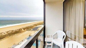 Un balcon donnant sur la plage, une chaise en plastique blanche et une paroi en verre.