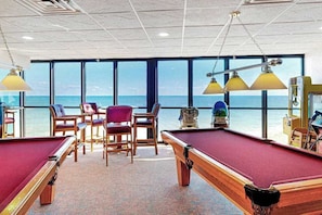 A pool table area with chairs and a view of the ocean. - Sunny, beachfront studio with balcony, full kitchen, AC, pools, tennis & gym (Ocean City)