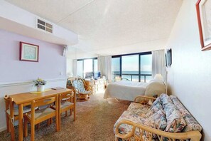 A hotel room with a bed, a dining table with chairs, a sofa, and a view of the ocean. - Beachfront studio with small balcony, AC, pools, gym, game room & sauna (Ocean City)