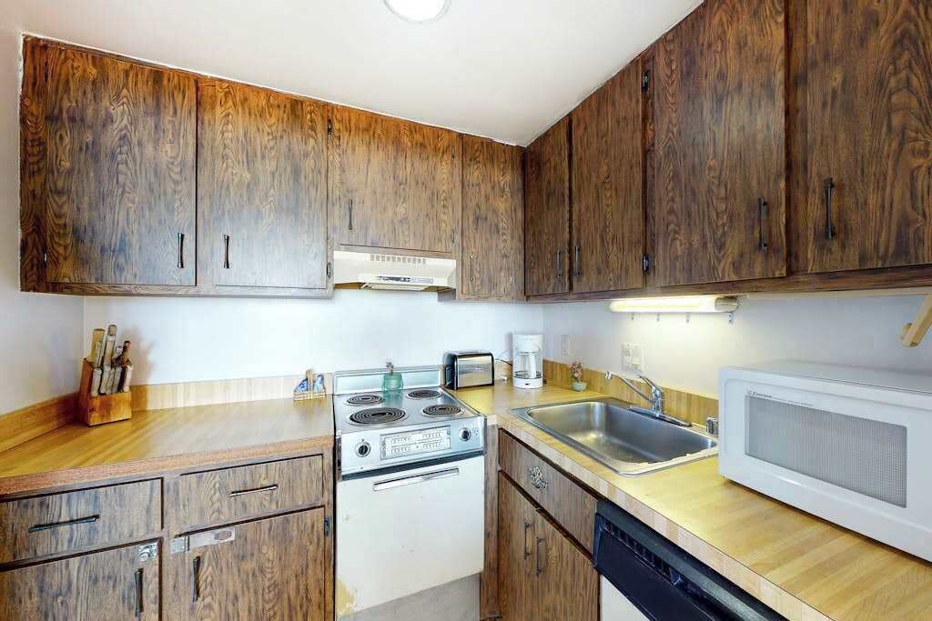 Een keuken met houten kastjes, een fornuis, een spoelbak en een magnetron.
