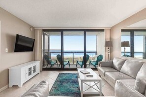 Ein Wohnzimmer mit einer Couch, einem Couchtisch, einem Fernseher und Meerblick durch große Fenster.